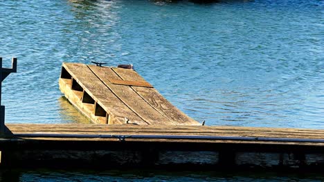 Old-Wooden-boat-dock-in-port-with-no-boat-attached-in-sunny-blue-water