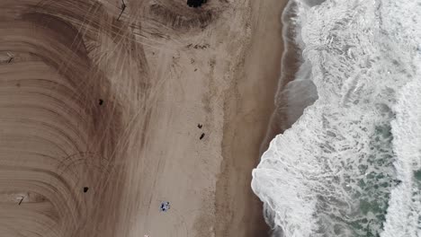 Birdseye-view-drone-footage-of-a-beautiful-beach-with-waves-crashing-against-the-soft-white-sand
