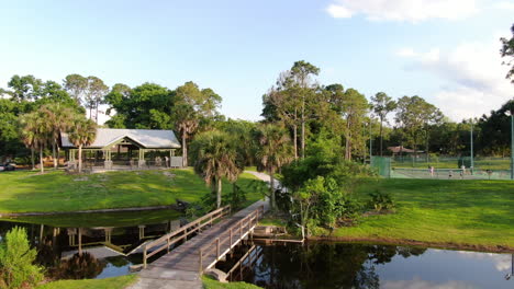 Pan-Up-from-Lakeside-Park-with-Bridge,-Stream,-Tennis-Courts-and-Gazebo