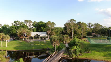 Lakeside-Park-with-a-Wooden-Bridge-over-a-Stream,-with-Tennis-Courts-and-Gazebo