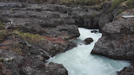 Panning-and-tilding-footage-of-the-rivers-coming-from-Barnafoss-waterfall-also-showing-a-viewing-platform-in-Iceland