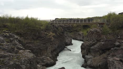 Panning-and-tilding-footage-of-the-rivers-coming-from-Barnafoss-waterfall-also-showing-a-viewing-bridge
