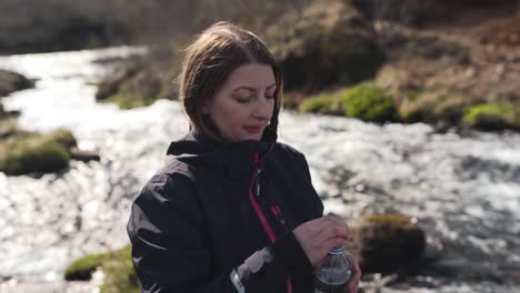 Female-hiker-just-filled-her-bottle-with-fresh-water-from-a-river-coming-from-Bruarfoss-in-Iceland-and-taking-a-sip-of-it