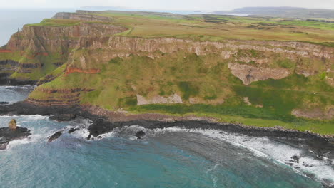 Aerial-dolly-shot-of-steep-cliffs-and-oceanic-waves-splashing-at-the-rocky-coastline-of-Northern-Ireland