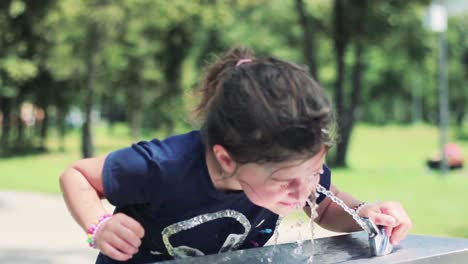 Little-girl-washes-her-face-and-drink-cool-water-from-a-drinking-fountain,-on-a-hot-summer-day