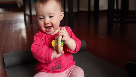 Cute-little-baby-smiles-and-plays-with-a-wood-toy-in-front-of-the-camera,-shot-in-slow-motion