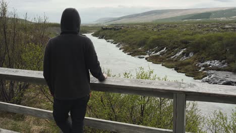 Handsome-young-male-with-a-hoodie-looking-at-a-beautiful-view-at-Barnafoss-waterfall-in-Iceland-all-alone-and-waiting-for-someone