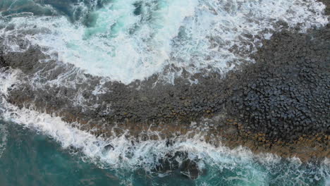 Static-top-down-view-of-oceanic-waves-splashing-at-the-shore's-rock-formation-in-Northern-Ireland