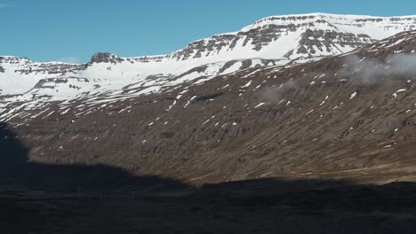 Schwenk-Von-Rechts-Nach-Links-Zeigt-Einige-Schneebedeckte-Berge-Und-Eine-Straße,-Die-Durch-Die-Berge-In-Island-In-Der-Nähe-Von-Gufufoss-Führt