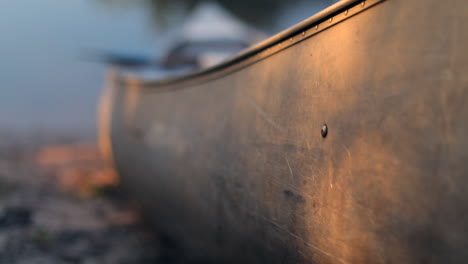 Used-and-scratched-metal-canoe-on-side-of-river-during-sunset