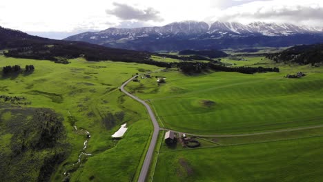 Drone-shot-over-a-road-and-green-fields-with-snowy-mountains-ahead
