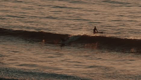 Two-surfers-in-the-water-during-sunset-in-slow-motion