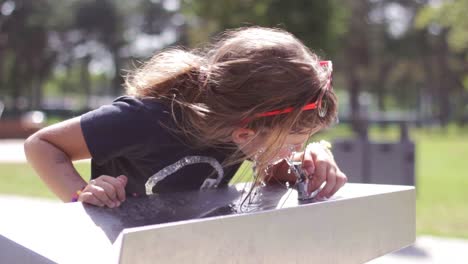 Little-girl-washes-her-face-and-drink-cool-water-from-a-drinking-fountain,-on-a-hot-summer-day-1