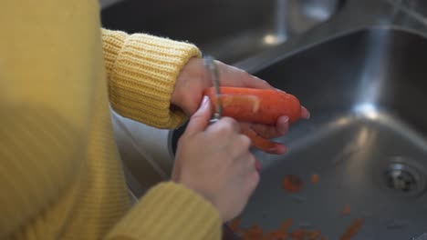 Closeup-footage-of-a-woman-wearing-a-yellow-sweater-peeling-a-fat-carrot-with-a-peeler-over-the-sink