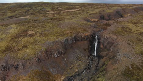 Aerial-footage-closing-up-on-a-majestic-waterfall-located-in-the-mountains-of-Iceland