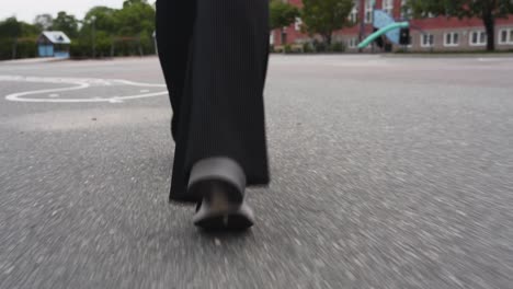 Closeup-moving-footage-following-the-feet-of-a-female-walking-on-a-school-yard-on-asphalt