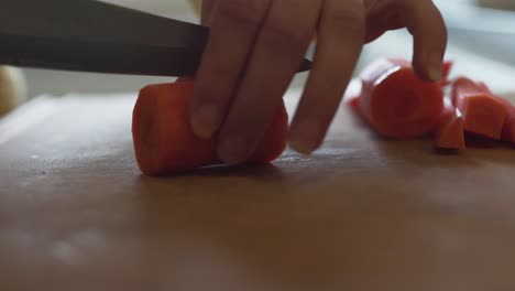 Closeup-of-woman-in-a-kitchen-using-a-sharp-knife-to-slice-a-carrot-into-pieces
