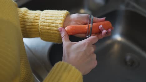 Closeup-footage-of-a-woman-wearing-a-yellow-sweater-peeling-a-carrot-with-a-peeler-over-the-sink