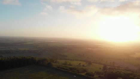 Aerial-cinematic-shot-of-english-country-road-in-green-countryside-during-sunset-with-bright-orange-glow-1
