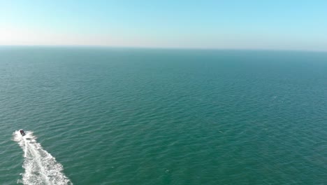 Cinematic-aerial-drone-shot-of-speedboat-sailing-into-distance-across-deep-blue-sea-on-english-coastline-on-sunny-summers-day-with-clear-blue-sky