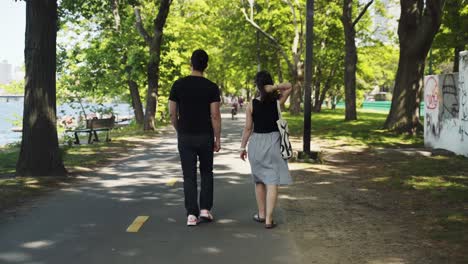 Rear-View-Of-Couple-Walking-Along-Path-By-Park