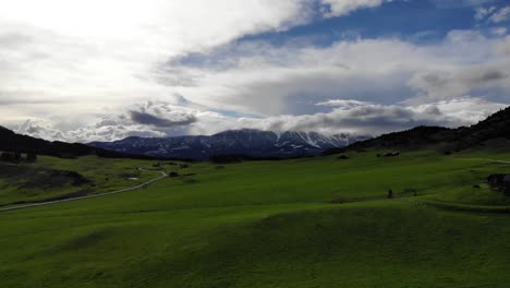 A-drone-shot-of-snowy-mountains-contrasted-with-green-rolling-plains