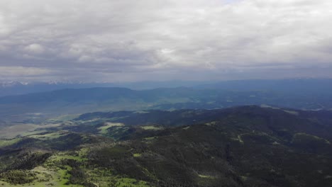 Drone-De-Gran-Altitud-De-Colinas-Verdes,-Pinos-Y-Montañas-En-El-Fondo