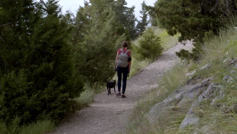 Woman-walking-a-small-black-dog-on-a-hiking-trail