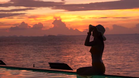 Silhouette-of-woman-sitting-by-the-poolside-with-twilight-background