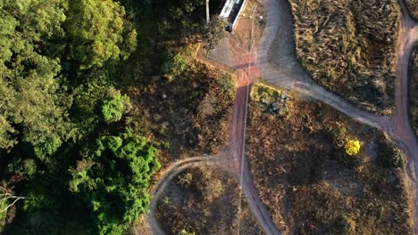 HD-aerial-drone-footage-of-trees-and-dirt-road-in-Brasilia,-Brazil-near-Lake-Paranoa-with-birds-flying-by-underneath