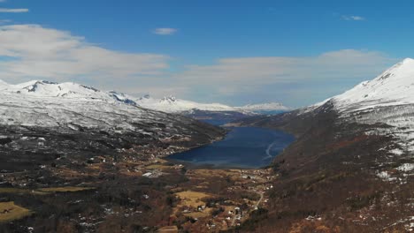 Panoramic-aerial-of-a-beautiful-valley-in-between-snowy-mountains-during-spring