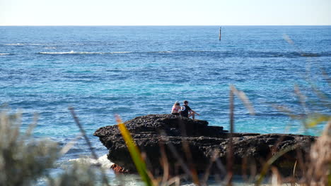 Two-people-romantically-on-rocks-next-to-water's-edge