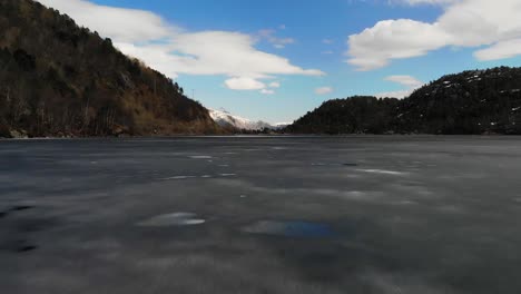 Drohne-Fliegt-In-Der-Nähe-Eines-Zugefrorenen-Sees-Mit-Bergigem-Hintergrund