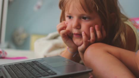 Close-up-of-a-cute-little-girl-laying-on-the-bed-and-watching-cartoons-on-laptop
