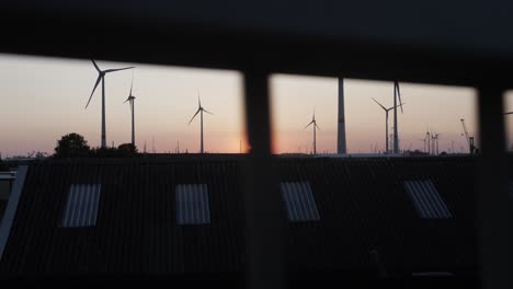 Cinematic-slow-motion-shot-behind-a-railing,-view-of-the-sunset-with-wind-turbines-in-the-background