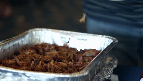 Cooked-seasoned-marinated-pulled-pork-gets-put-on-man's-plate-with-plastic-fork