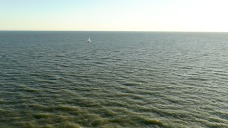 Aerial-view-of-a-sailboat-in-the-distance-sailing-across-the-ocean