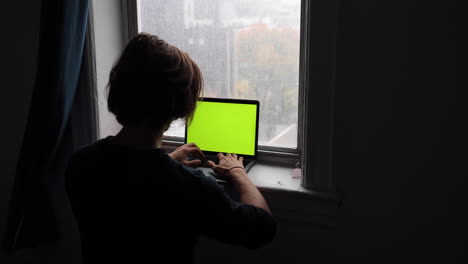 Young-man-types-and-work-on-his-laptop-in-front-of-a-beautiful-window-view