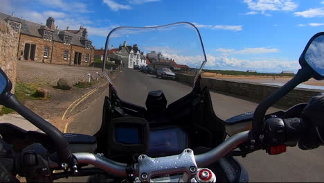 Biker-riding-a-motorcycle-to-a-harbour-in-Scotland-with-clear-blue-skies-and-yachts-in-the-marina