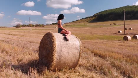Aerial-shot-of-beautiful-brunette-sunbathing-while-sitting-on-a-bale-of-hay