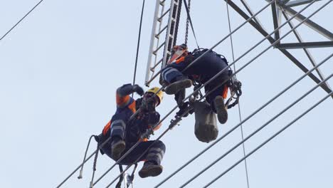 Two-maintenance-technicians-sit-high-up-on-power-lines
