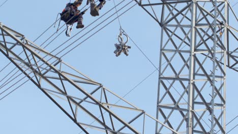 Two-workers-sit-on-high-power-voltage-cables-hoist-equipment-up