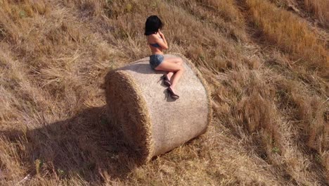 Orbital-shot-of-beautiful-brunette-woman-sitting-in-bale-of-hay-posing-under-the-sun