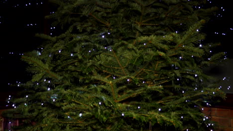 Neigen-Sie-Den-Weihnachtsbaum-Mit-LED-Lichterketten-Mit-Lichtreflexionen-An-Den-Fenstern-Im-Hintergrund