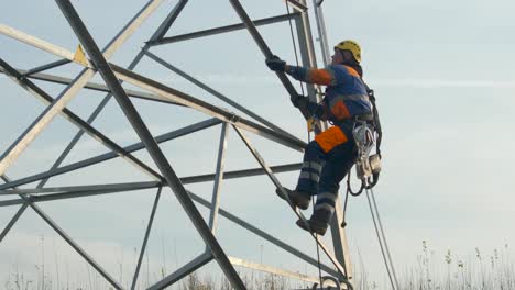 Electrical-engineer-with-dangerous-job-climbs-up-pylon,-wearing-safety-harness