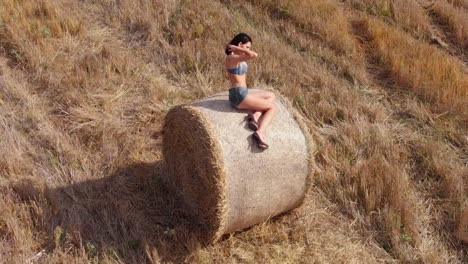 Orbital-shot-of-pretty-young-woman-playing-with-her-hair-while-sitting-in-bale-of-hay