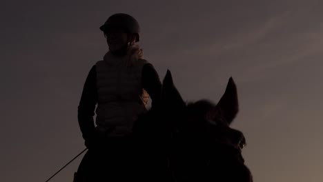 Beautiful-silhouette-rider-mounted-on-grazing-horse-at-sunset,-medium