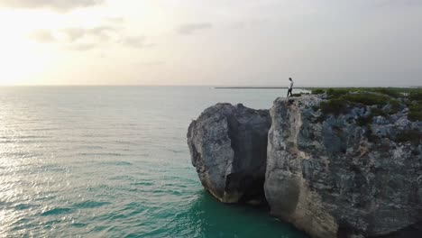 Young-male-walking-along-a-rocky-cliff-on-the-ocean-in-Providenciales-in-the-Turks-and-Caicos-archipelago-at-sunset