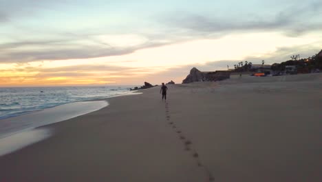 Young-male-running-along-a-sandy-beach-in-Cabo-San-Lucas,-Mexico,-at-sunset