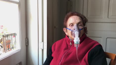 Surrounding-a-caucasian-elderly-woman-sitting-by-a-window-with-mask-receiving-nebulizer-treatment